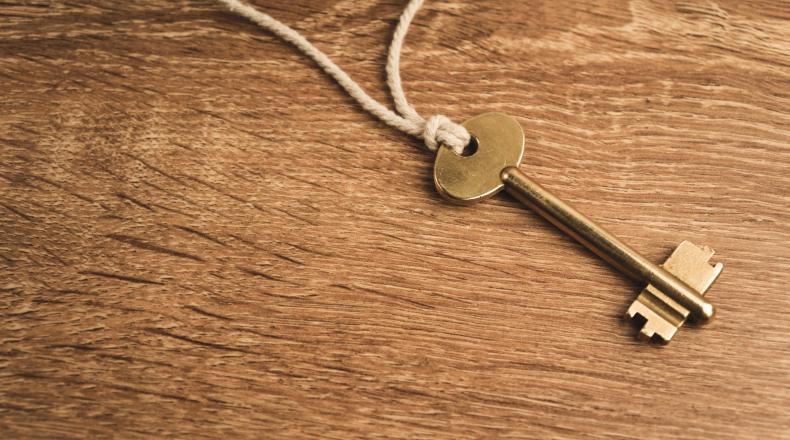 Golden key on rope on wooden background
